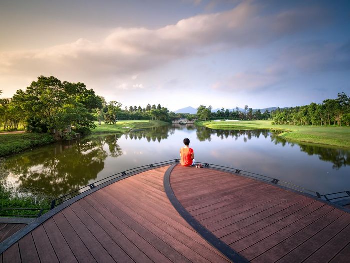 Person meditating peacefully outdoors near a calm lake at sunrise.